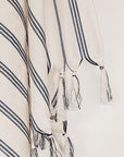 Close-up image of a beige towel with vertical blue & black stripes colours and knotted fringe.