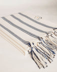Side image of a beach towel with vertical blue & black stripes colours and knotted fringe.