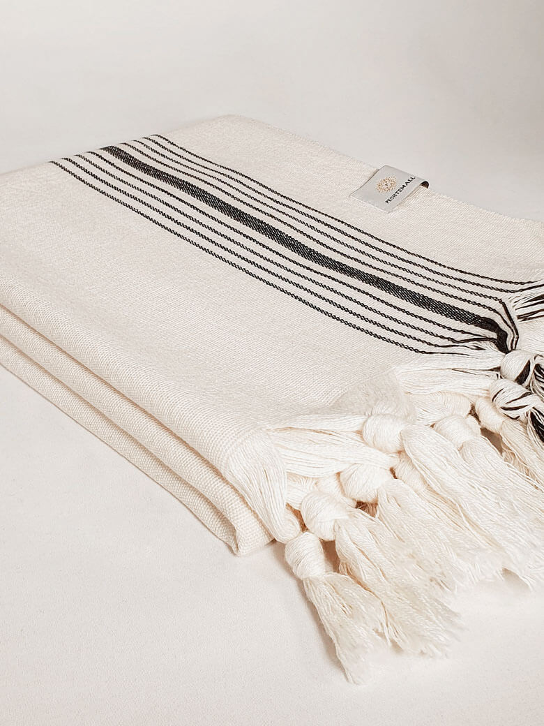 Side image of folded plain beige hammam towel with vertical black stripes.