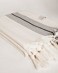 Side image of folded plain beige hammam towel with vertical black stripes.