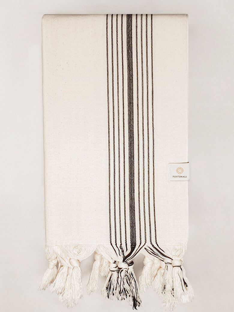 Folded plain beige hammam towel with vertical black stripes and knotted fringe.